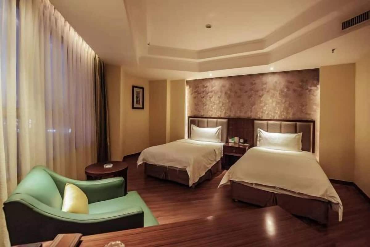 A hotel room with two beds, a green sofa, a small table, and a large window with curtains.
