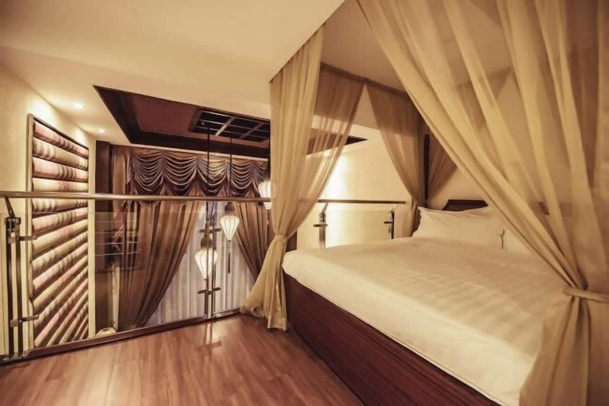 A bedroom with a bed, curtains, a mirror, and a wooden floor.