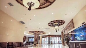 Un hall d’entrée spacieux avec un plafond haut, des lustres modernes, un grand aquarium et des coins salons confortables.