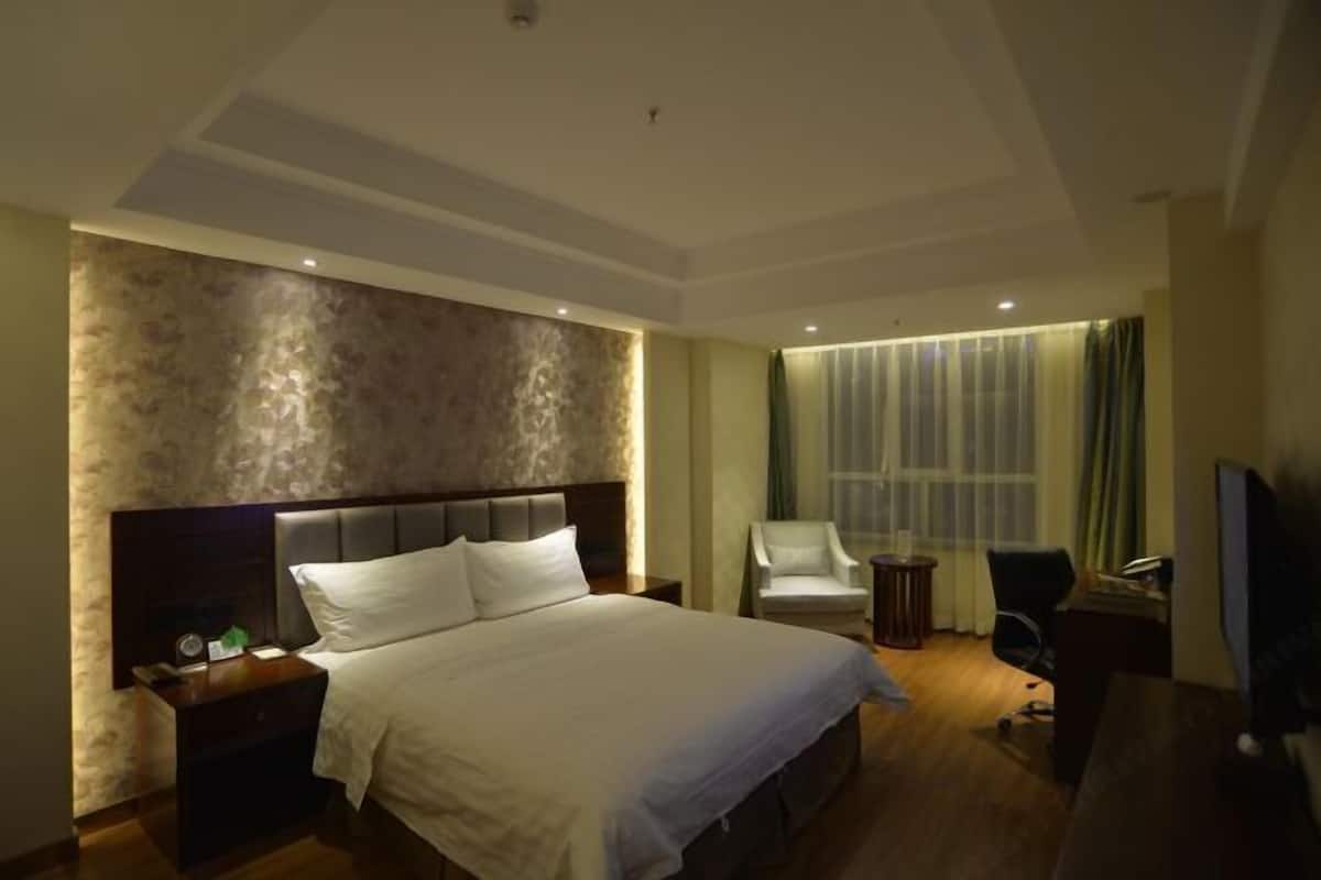 A hotel room with a large bed, a desk, a chair, and a TV.