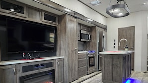 Una cocina moderna con televisor integrado, microondas, horno y una pequeña isla con pileta.