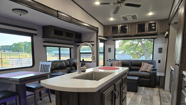 Cocina moderna para vehículos recreativos con una isla central, zona de comedor y espacio de estar con vistas al exterior.