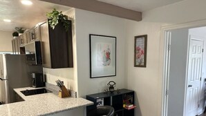 A kitchen with a granite countertop, stainless steel appliances, and a black bar stool. There are framed pictures on the wall and a door leading to another room. - LUXURY 2-bedroom house in brilliant Bisbee with BREATHE taking views (Bisbee)