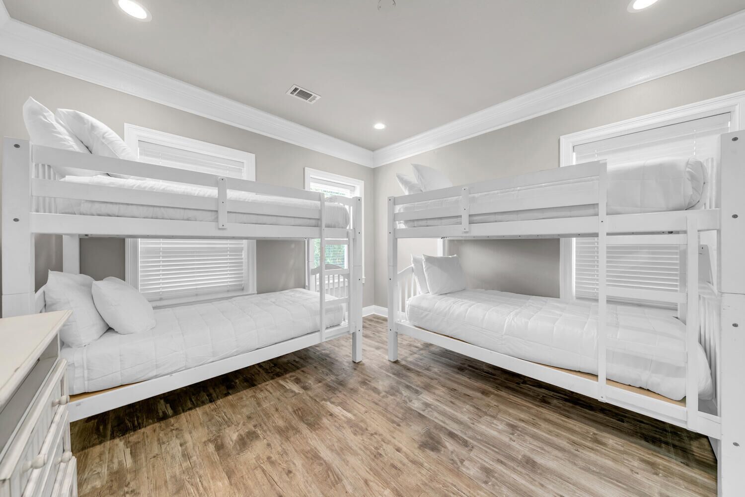 A room with two bunk beds, wooden flooring, and a window with blinds.