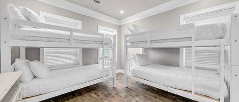 A room with two bunk beds, wooden flooring, and a window with blinds.