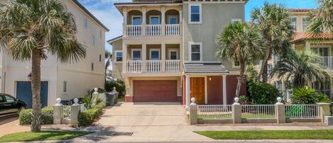 A two-story residential building with a garage, a balcony on the upper floor, and a well-maintained front yard with palm trees.