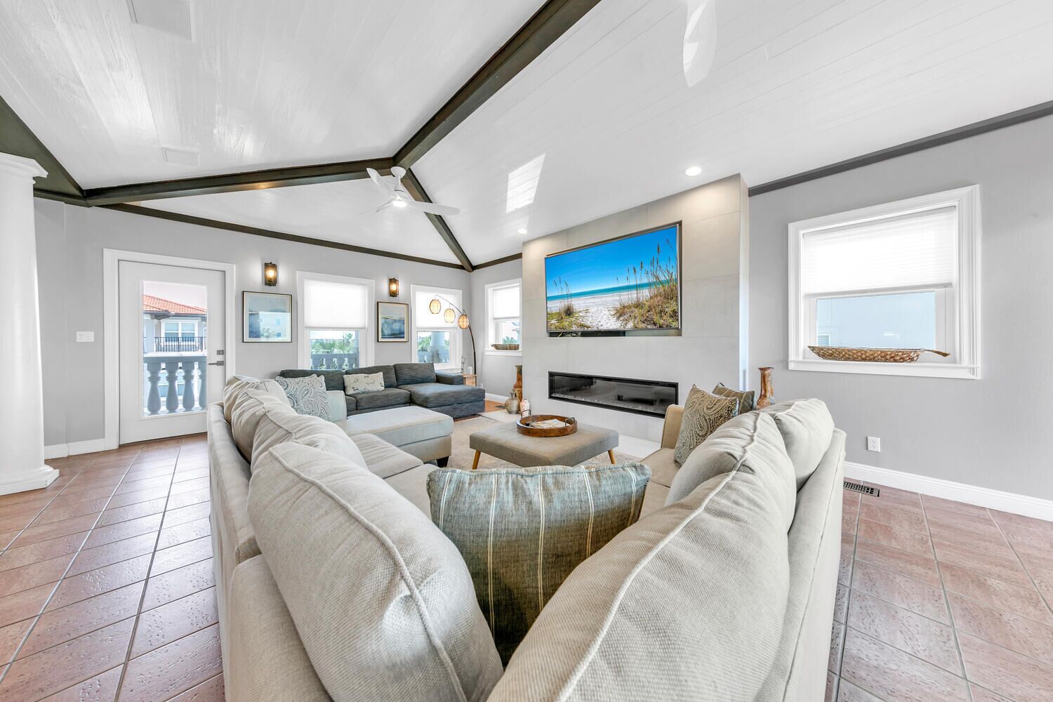 A spacious living room with a large sectional sofa, a fireplace, and a large window with a beach view.