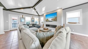 A spacious living room with a large sectional sofa, a fireplace, and a large window with a beach view.