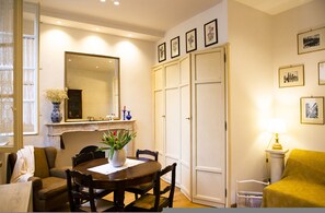 A dining area with a round table, chairs, a vase with flowers, a mirror, and framed pictures on the wall. - Welcomely - Burlamacchi House (Lucca)