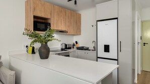 A modern kitchen with white cabinetry, a central island, a microwave, and a refrigerator. - The Sage - Elegant Studio in Vibrant Sea Point (Cape Town)