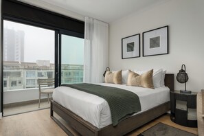 Relax in this serene hotel room with a large bed, framed artwork, and a city view through the window.