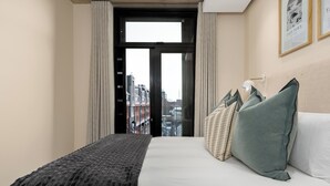 Ett hotellrum med en stor säng, utsikt över staden genom en glasdörr och en inramad tavla på väggen.