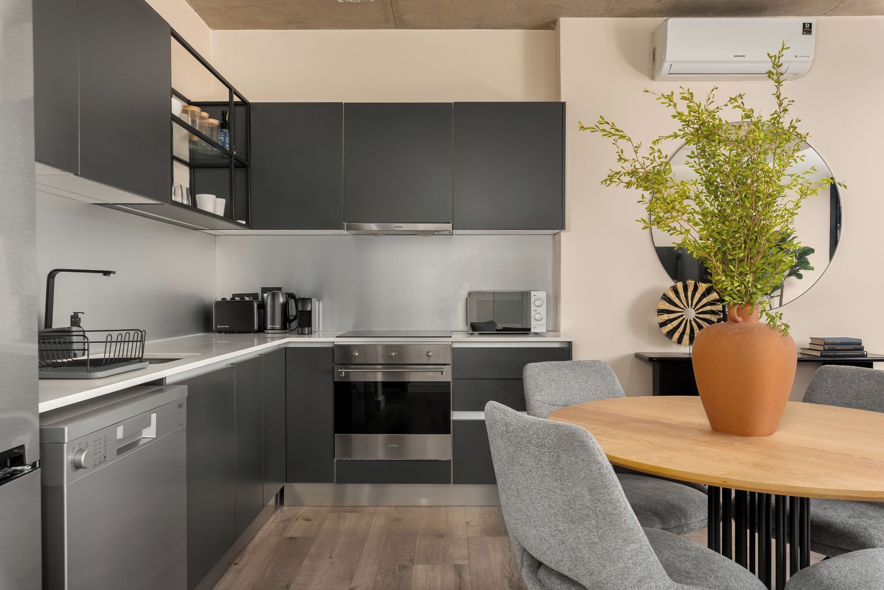 A modern kitchen with grey cabinets, stainless steel appliances, and a round wooden table with grey chairs.