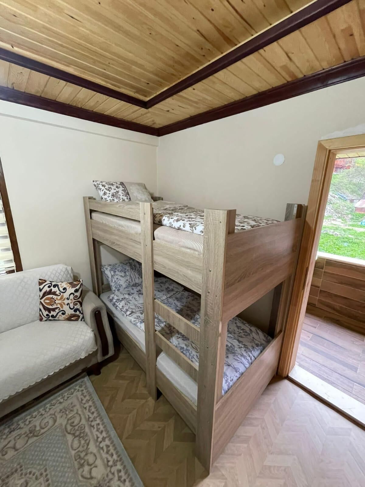 A bunk bed with a wooden frame and patterned bedding, a sofa with a patterned cushion, and a herringbone-patterned floor.