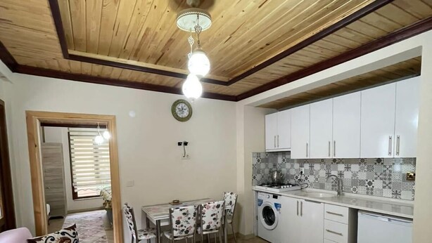 Una sala de estar acogedora con un sofá, una mesa de comedor con sillas, una cocina con armarios blancos y una alfombra estampada.