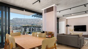 A modern living room with a dining area, large windows, and a view of buildings and mountains.
