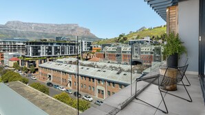 A balcony with a view of a cityscape, including modern buildings and a distant mountain.
