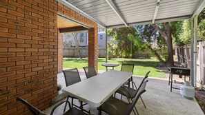 A covered patio with a brick wall, a table with chairs, and a view of a backyard with a fence and trees.