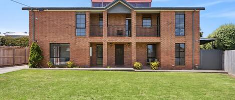 A two-story brick house with a front porch, a small front yard, and a fenced backyard.