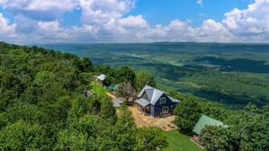 Una casa con techo inclinado rodeada de abundante vegetación y una vista panorámica de colinas ondulantes.