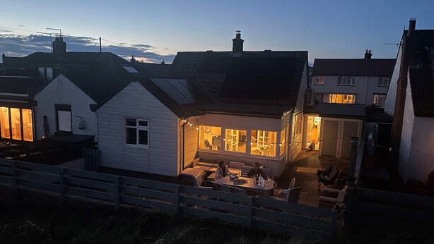 A white house with a dining area and a visible window. - Marram Cottage - Cosy, well equipped, family, beach house (Chathill)