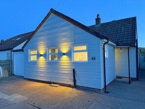 A single-story house with a gabled roof, a garage door, and a small porch. - Marram Cottage - Cosy, well equipped, family, beach house (Chathill)