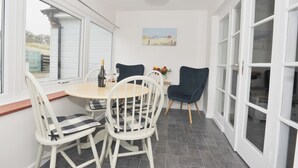 A dining area with a round table, white chairs, and a vase of flowers. - Marram Cottage - Cosy, well equipped, family, beach house (Chathill)