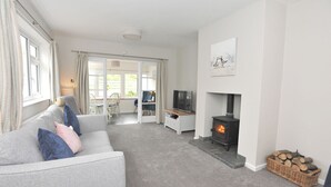 A modern living room with a grey sofa, a fireplace, and a television. - Marram Cottage - Cosy, well equipped, family, beach house (Chathill)