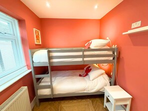 A bunk bed with white bedding, a white bedside table, and a radiator.