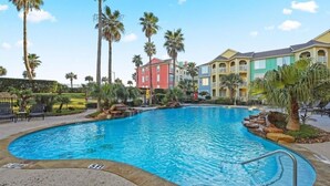 A swimming pool surrounded by palm trees and colorful buildings. - Charming BEACHFRONT condo in Galveston, 2 POOLS open year round, FITNESS CENTER (Galveston)