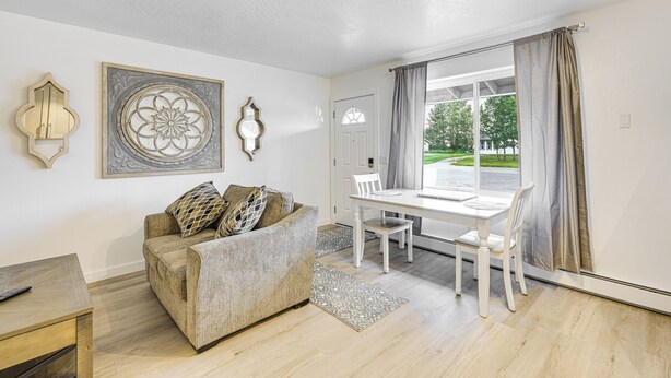 Ein Wohnzimmer mit einer Couch, einem Esstisch und Stühlen. An den Wänden befinden sich dekorative Elemente und ein Fenster mit Vorhängen.