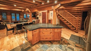 A log cabin interior with a kitchen, dining area, and a staircase.