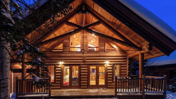 A log cabin with a large porch and multiple windows, surrounded by snow.