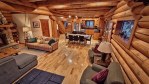A log cabin interior with a living room, dining area, and kitchen.
