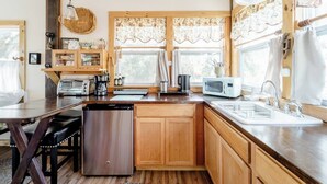 A compact kitchen with wooden cabinets, a stainless steel dishwasher, a built-in microwave, and a coffee maker. - Charming cottage on the ORANGE RIVER in Fort Myers Fl. Pool ,Kayaks, AC, WiFi (Fort Myers)