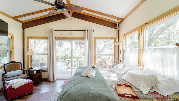 A spacious bedroom with a large bed, a wooden ceiling fan, and a view of the outdoors through large windows. - Charming cottage on the ORANGE RIVER in Fort Myers Fl. Pool ,Kayaks, AC, WiFi (Fort Myers)