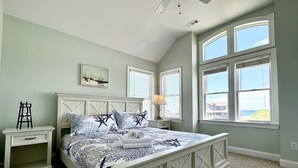 Ein Schlafzimmer mit einem Bett, Nachttischen, einem Deckenventilator und groĂen Fenstern.