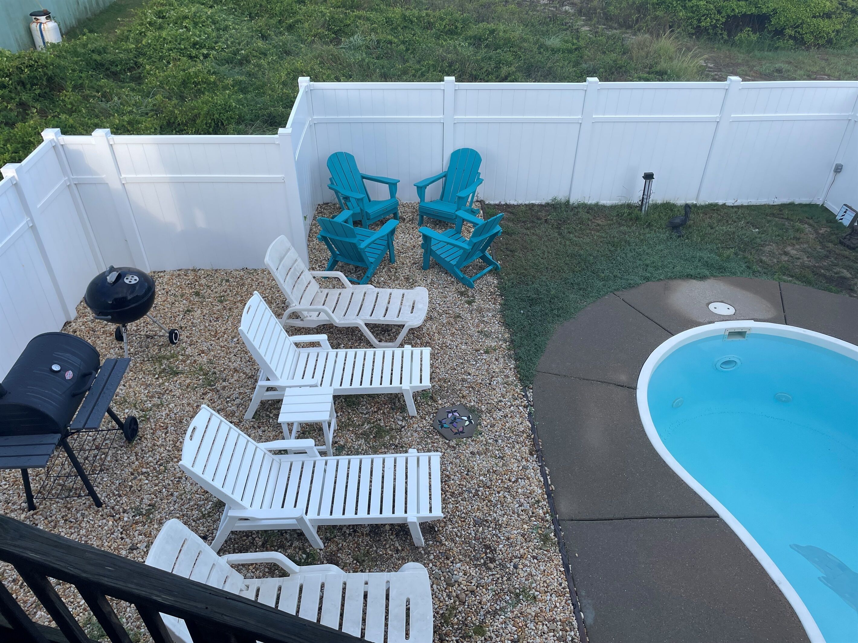 Un jardin avec une piscine, des chaises longues blanches et un espace barbecue.