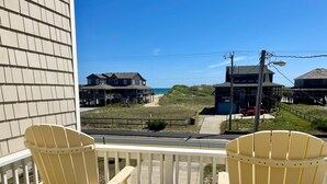 Ein Balkon mit zwei gelben Adirondack-StĂŒhlen und einem kleinen violetten Tisch, mit Blick auf einen Strand mit HĂ€usern und einer StraĂe.