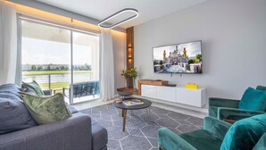 A modern living room with a sofa, armchairs, a coffee table, and a TV mounted on the wall. - Stylish 2-br Apt Sleeps 7 Near Disney Magic (Kissimmee)