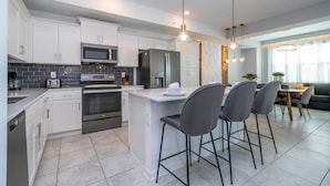 A modern kitchen with white cabinets, stainless steel appliances, and a central island with bar stools. - Stylish 2-br Apt Sleeps 7 Near Disney Magic (Kissimmee)