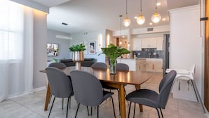 A modern dining area with a wooden table, black chairs, and pendant lighting. - Stylish 2-br Apt Sleeps 7 Near Disney Magic (Kissimmee)