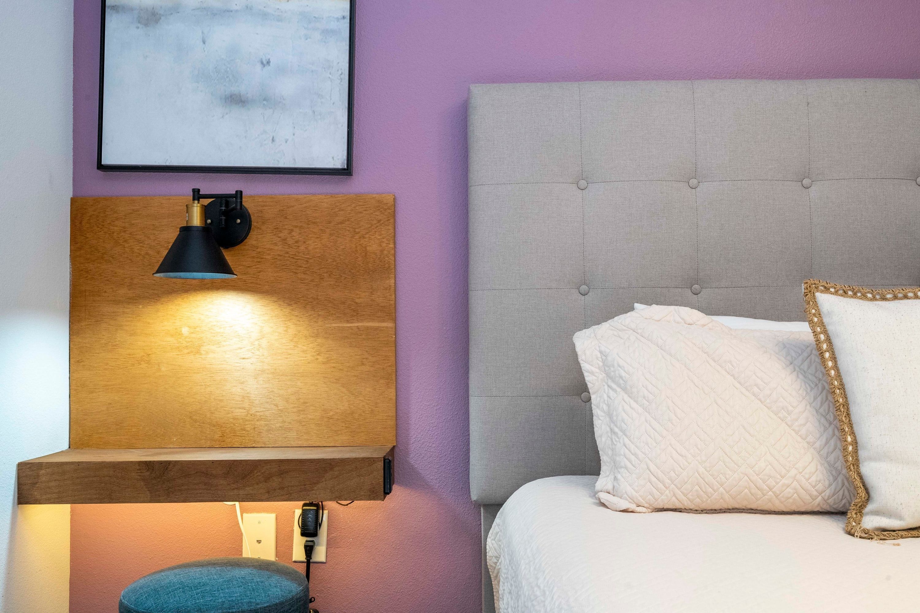A bedroom with a tufted headboard, a bedside lamp, a framed picture, and a bedside table.