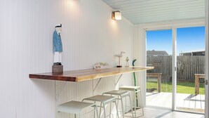 Eine Küche mit einer Holzausziehtafel, weißen Barhocker und einer Glasschiebet ür, die auf eine Terrasse führt.
