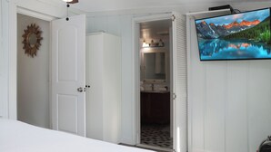 Ein Schlafzimmer mit einem Bett, einem an der Wand montierten Fernseher und einer Tür zu einem Badezimmer.