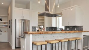 A modern kitchen with white cabinetry, stainless steel appliances, and a wooden bar stool area. - Rejuvenation:Brand New, Beach Views, Custom Furniture, Hot Tub + MIL Suite (St. Joe Beach)