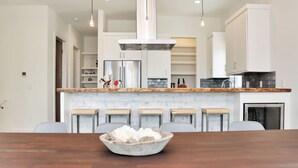 A modern kitchen with a central island, stainless steel appliances, and a dining area with a wooden table and bar stools. - Rejuvenation:Brand New, Beach Views, Custom Furniture, Hot Tub + MIL Suite (St. Joe Beach)