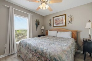 A bedroom with a bed, a ceiling fan, a window with curtains, a nightstand, and a wall-mounted lamp.