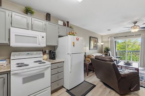 A compact kitchen with a stove, microwave, and refrigerator, adjacent to a seating area with a sofa and a dining table. - 1 BR | Whispering Pines | Indoor Pool | Mountain and D'town View (Pigeon Forge)