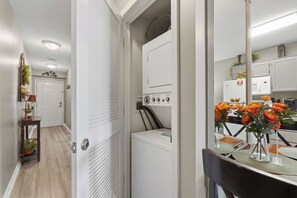 A laundry room with a washing machine, dryer, and a mirror reflecting a kitchen area with a microwave and a refrigerator.